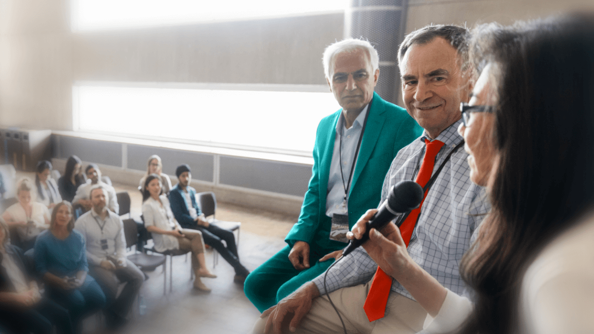 Photo of an event with a panel on stage having a discussion and an audience watching